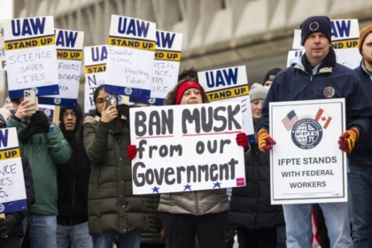 Protesters holding signs opposing Elon Musk’s government involvement, including a sign reading 'Ban Musk from our Government.' UAW and IFPTE union members participating in demonstration.
