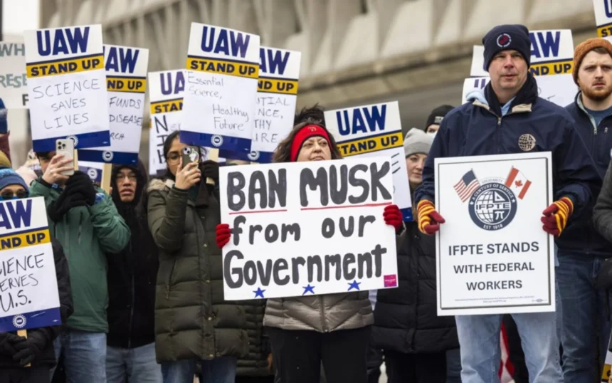 Protesters holding signs opposing Elon Musk’s government involvement, including a sign reading 'Ban Musk from our Government.' UAW and IFPTE union members participating in demonstration.