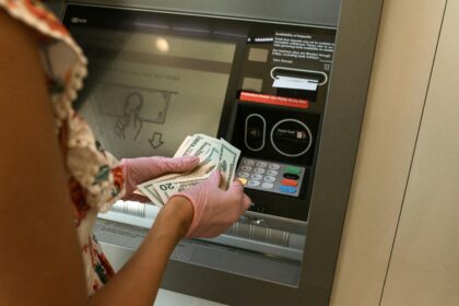 Person wearing gloves withdrawing cash from an ATM.