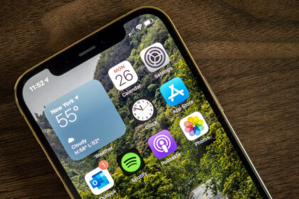 Close-up of iPhone 12 Pro home screen showing apps and weather widget on wooden table