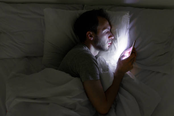 young man using phone in bed late at night