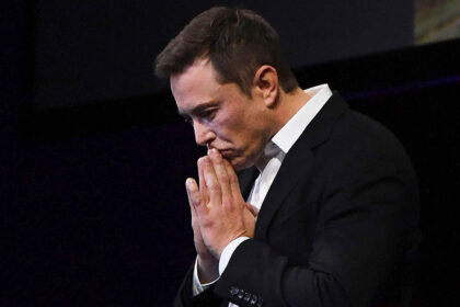 Elon Musk in deep thought, hands clasped in front of his face.